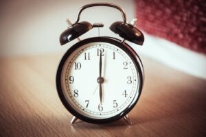 Classic black alarm clock on a wooden table, showing seven o'clock.