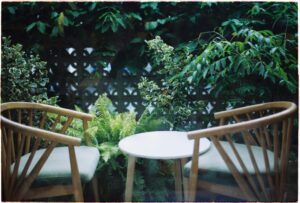 Charming outdoor area with wooden chairs and a table surrounded by greenery, perfect for relaxation.